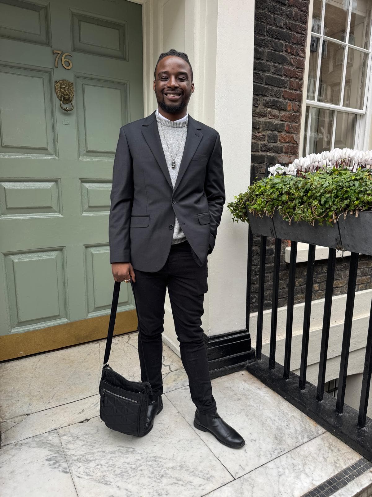 Emperor Roy standing outside 76 Dean Street, Soho House, suited and professional